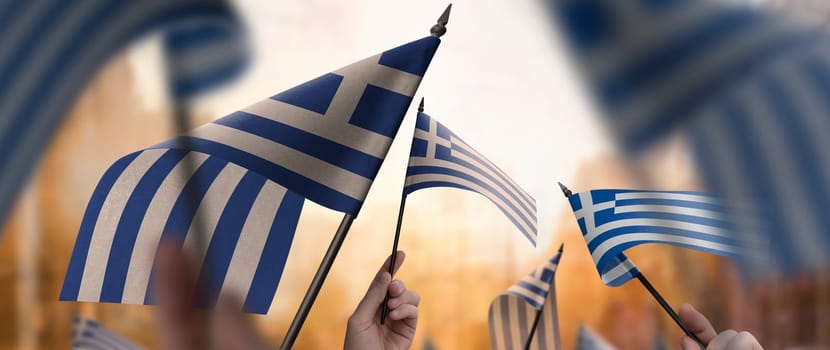 Greece flags in their hands on a blurred urban background. The photo illustration was created without the use of artificial intelligence, only using Photoshop.