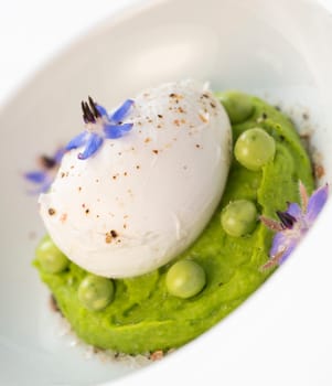 A fresh pea puree is beautifully plated, featuring a poached egg at the center and adorned with borage flowers. The dish showcases vibrant colors and textures, perfect for any spring menu.