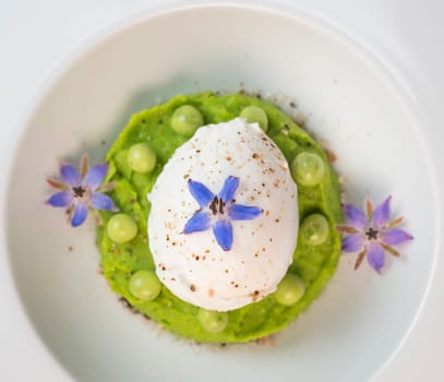 A fresh pea puree is beautifully plated, featuring a poached egg at the center and adorned with borage flowers. The dish showcases vibrant colors and textures, perfect for any spring menu.