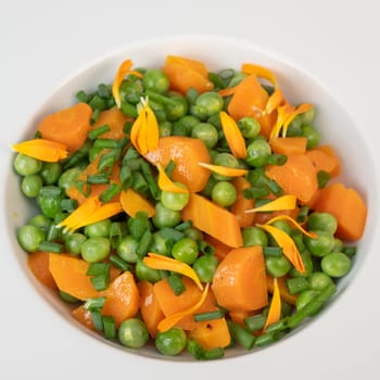 Fresh garden peas and carrots are cooked with salted butter, then garnished with chives and bright marigold flowers for an appealing and colorful side dish.