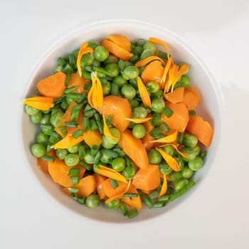 Fresh garden peas and carrots are cooked with salted butter, then garnished with chives and bright marigold flowers for an appealing and colorful side dish.