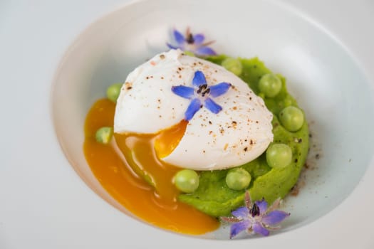 A fresh pea puree is beautifully plated, featuring a poached egg at the center and adorned with borage flowers. The dish showcases vibrant colors and textures, perfect for any spring menu.