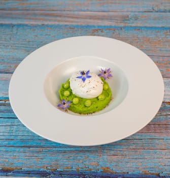 A fresh pea puree is beautifully plated, featuring a poached egg at the center and adorned with borage flowers. The dish showcases vibrant colors and textures, perfect for any spring menu.