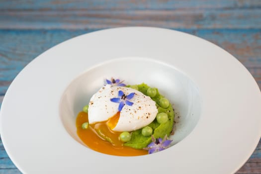 A fresh pea puree is beautifully plated, featuring a poached egg at the center and adorned with borage flowers. The dish showcases vibrant colors and textures, perfect for any spring menu.