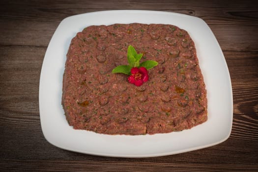 Kebbe naye is showcased on a white plate, featuring finely chopped raw meat mixed with bulgur, onions, mint, and spices, designed for a rich culinary experience.