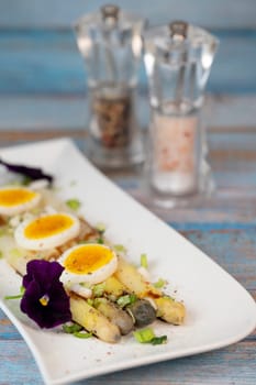 Baked asparagus with boiled egg in big white plate on blue background. High quality photo