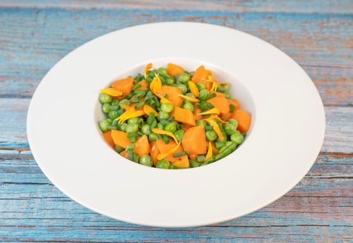 Fresh garden peas and carrots are cooked with salted butter, then garnished with chives and bright marigold flowers for an appealing and colorful side dish.