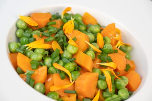 Fresh garden peas and carrots are cooked with salted butter, then garnished with chives and bright marigold flowers for an appealing and colorful side dish.