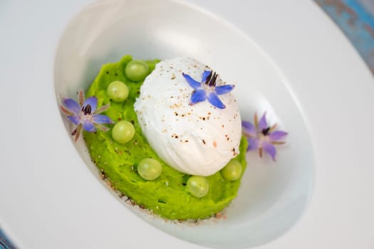 A fresh pea puree is beautifully plated, featuring a poached egg at the center and adorned with borage flowers. The dish showcases vibrant colors and textures, perfect for any spring menu.