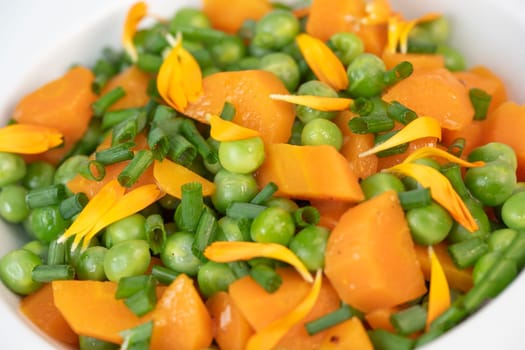 Fresh garden peas and carrots are cooked with salted butter, then garnished with chives and bright marigold flowers for an appealing and colorful side dish.