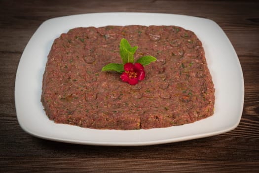 Kebbe naye is showcased on a white plate, featuring finely chopped raw meat mixed with bulgur, onions, mint, and spices, designed for a rich culinary experience.