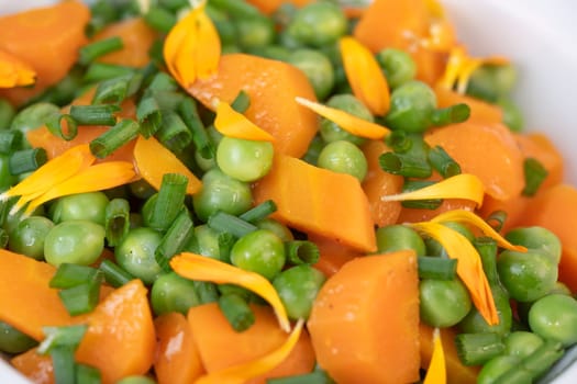 Fresh garden peas and carrots are cooked with salted butter, then garnished with chives and bright marigold flowers for an appealing and colorful side dish.