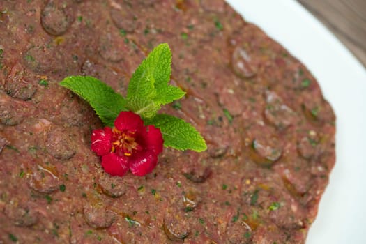 Kebbe naye is showcased on a white plate, featuring finely chopped raw meat mixed with bulgur, onions, mint, and spices, designed for a rich culinary experience.