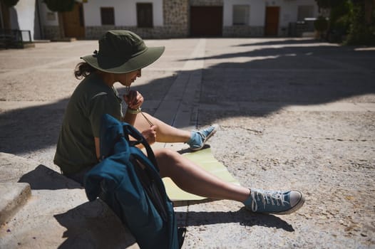 A person in casual attire sits on a plaza analyzing a map, showcasing scenic surroundings with a Mediterranean atmosphere.