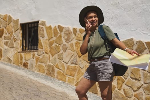 A traveler navigates a charming historic village, holding a map in hand while talking on the phone. The cobblestone pathway and rustic stone walls add to the picturesque ambiance.