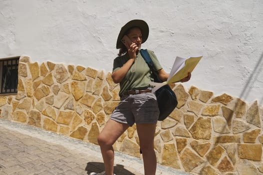 An enthusiastic traveler examines a map while exploring a historical stone village under the sunlight, showcasing a spirit of adventure and curiosity.