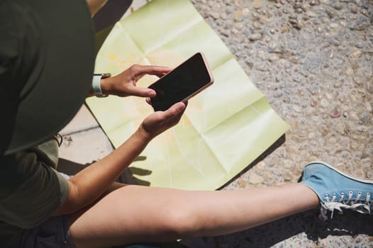 An individual examines their smartphone while sitting near an unfolded map of a historic city. The image captures a traveling moment filled with adventure and outdoor exploration.