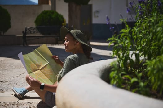 A tourist sits outdoors with a map, wearing a casual outfit. The setting is a scenic historic village surrounded by nature, offering a relaxing and explorative atmosphere.