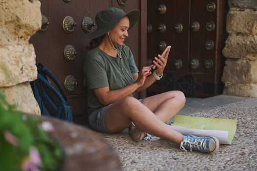 A solo traveler sits by a medieval city door, engaging with a phone and map. Ideal for wanderlust and outdoor adventure themes.