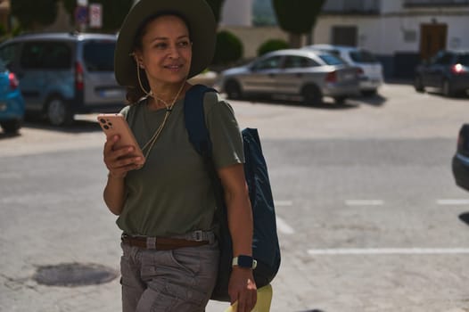 A traveler enjoys exploring a historic Spanish village surrounded by mountains, holding a smartphone. Her outdoorsy attire and smile convey the joy of discovery in scenic locations.