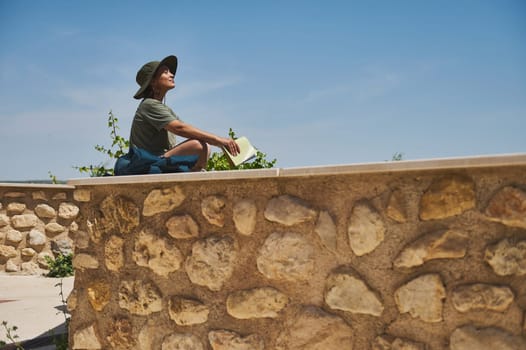 A traveler enjoys a sunny day in a Medieval Spanish village, holding a guide, ready to explore. The backdrop features rustic architecture and the mountains of the Cazorla ridge.