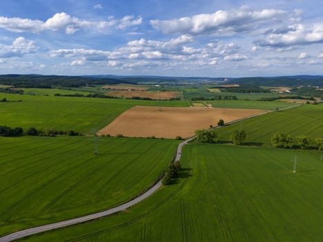 Road with cars between green fields from above - view of nature from a drone. Beautiful landscape concept suitable for transportation, agriculture and environment.