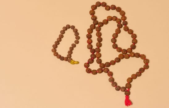 Top view of two strands of rudraksha beads, one of which is longer and has a red tassel, placed on a beige background
