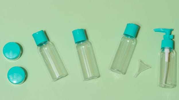 Top view of set of five transparent cosmetic bottles and two round jars with turquoise lids and one funnel, light green background