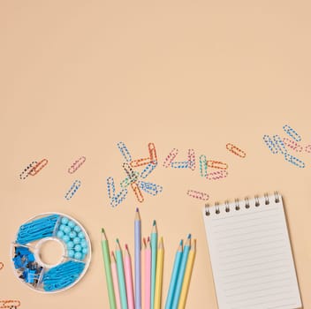 Flat lay of colorful school and office supplies including pencils, paper clips, notebooks on a peach background. Creative workspace concept.