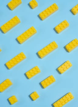Scattered yellow plastic toy building bricks on a blue background. Play, construction, education or creative concept