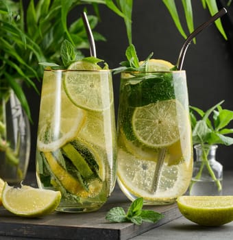 Refreshing detox or summer drink in a glass with lemon, lime, mint, ice, and metal straw. Dark background