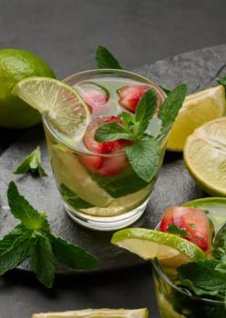 Refreshing mojito cocktail with lime, mint, strawberry, and ice on dark background, top view