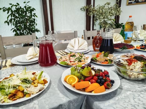 A table is laden with various salads, fruit plates, and drinks. A white tablecloth provides the backdrop for the diverse dishes at this festive meal, likely in a restaurant.
