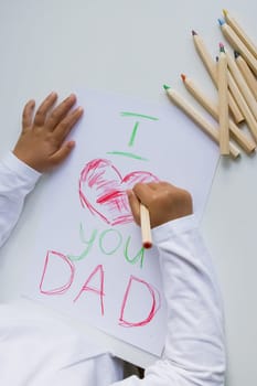 Child drawing I love you dad with colored pencils on white paper.