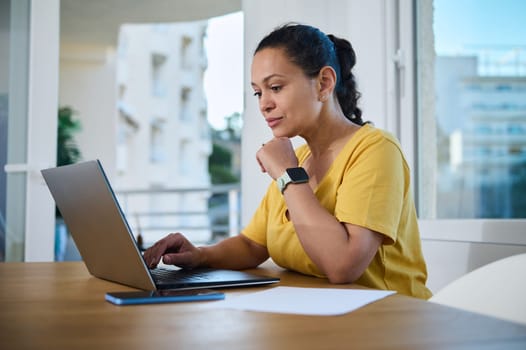 A focused woman working on her laptop at home, displaying productivity and modern technology in a comfortable environment.