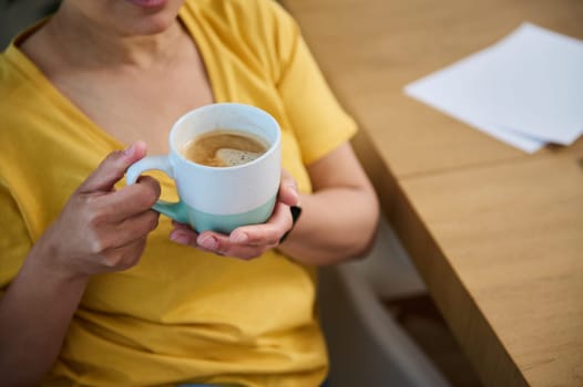 A person enjoying a warm cup of coffee during a restful moment indoors. The scene exudes comfort and relaxation with natural light emphasizing a peaceful atmosphere.