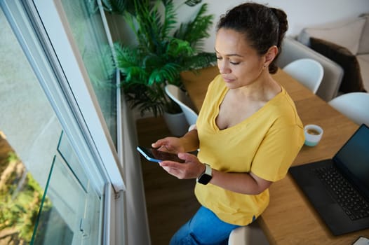 Confident woman engaged with her smartphone while working from her home office, highlighting modern communication and remote work. A serene and productive environment with personal balance and technology.