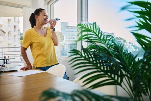 A cheerful woman interacts with her phone in a vibrant home office, embodying productivity and comfortable remote work.
