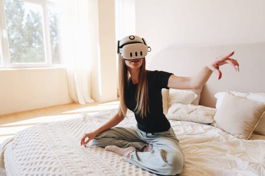 A young woman enjoys a virtual reality headset while seated on a cozy bed in a stylish, well-lit room. The atmosphere is relaxed as she interacts with her virtual environment.