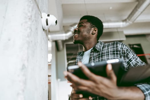 A young man, smiling and dressed casually, interacts with an innovative device mounted on a wall in a bright, modern office setting during the afternoon.
