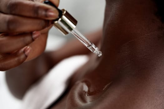 A person carefully applies a dropper of facial serum to their neck, showcasing the detailed skincare routine in a serene treatment space. Relaxation and self-care are evident.