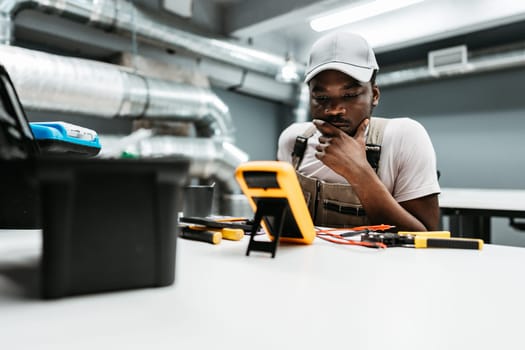 A young technician intently examines multimeter readings while seated at a workbench filled with tools during a training session in a workshop.