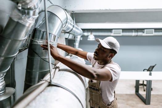 A technician carefully examines the ventilation ducts in a contemporary office setting. Wearing work attire, he ensures proper function and safety of the air system.
