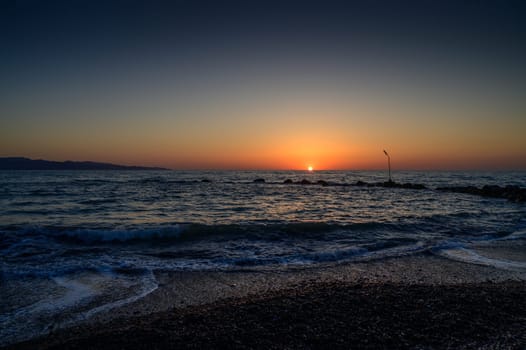 The sun sets into the calm waters of the Mediterranean Sea, casting warm reflec