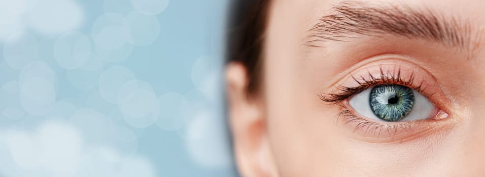 Focusing on a striking human eye with a vibrant blue iris and detailed eyelashes, complemented by a soft, blurred blue background. The image captures the beauty and intricacy of the eye.