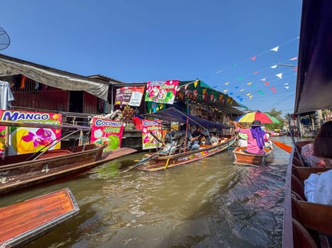 Bangkok, Thailand - November 12, 2024: Tourists on boats for the floating market, buying traditional Thai food or souvenirs from their sailboat on the canal. Famous marketplace on the water.