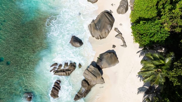 Boulders scattered across a white sandy beach with turquoise waters gently lapping the shore. Seychelles, Mahe. Carana Beach.