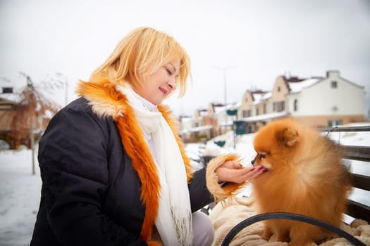A middle-aged woman lovingly interacts with her red Pomeranian dog while enjoying a snowy day outdoors.