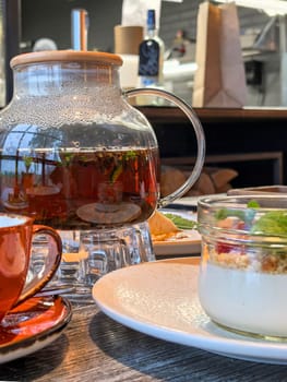 Tea brewed in a glass teapot is surrounded by a cup and a dessert jar. The setting offers a cozy atmosphere. Made on smartphone.