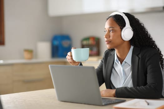 Black executive listening online audio drinking in the kitchen at home